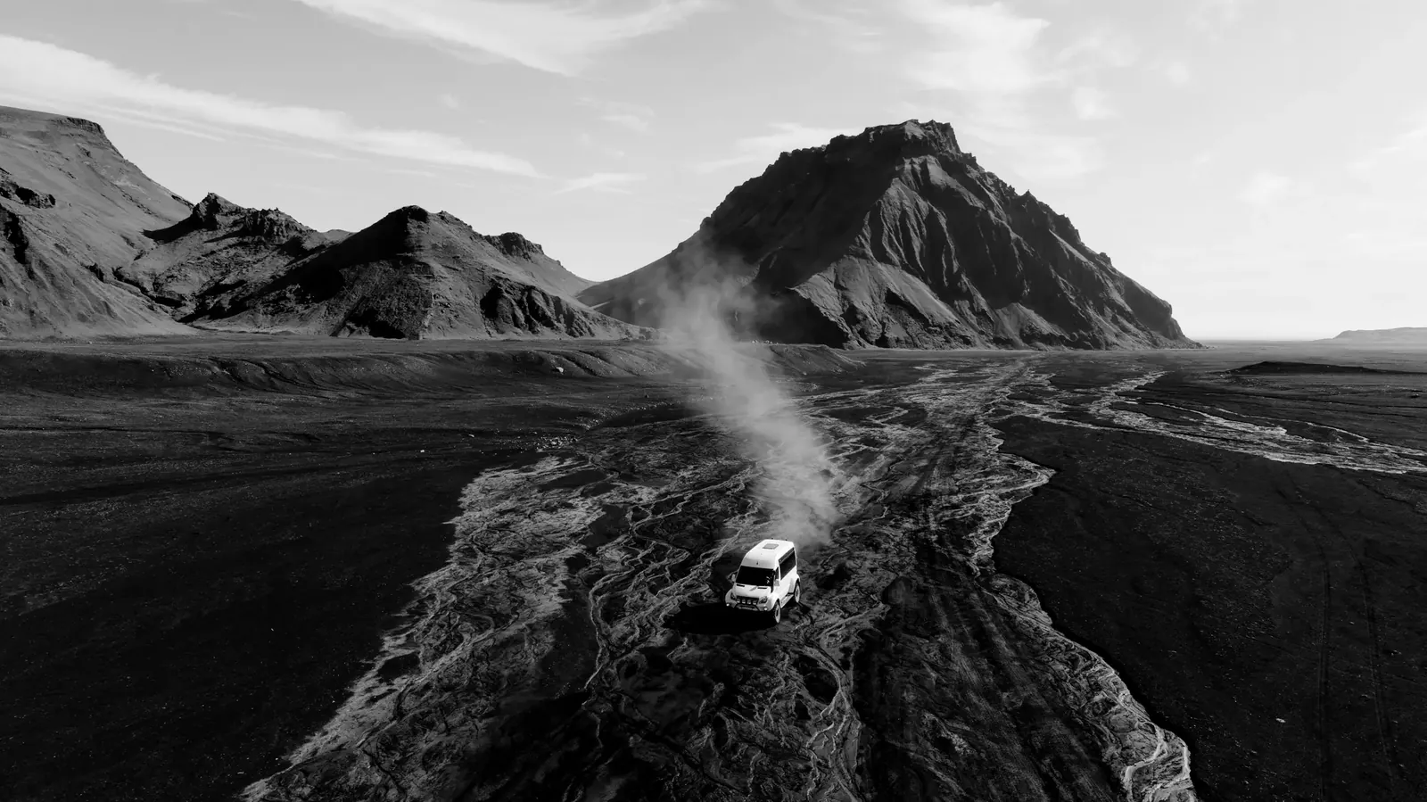 A 4x4 kicking up dust on a black sand track below a mountain in Iceland